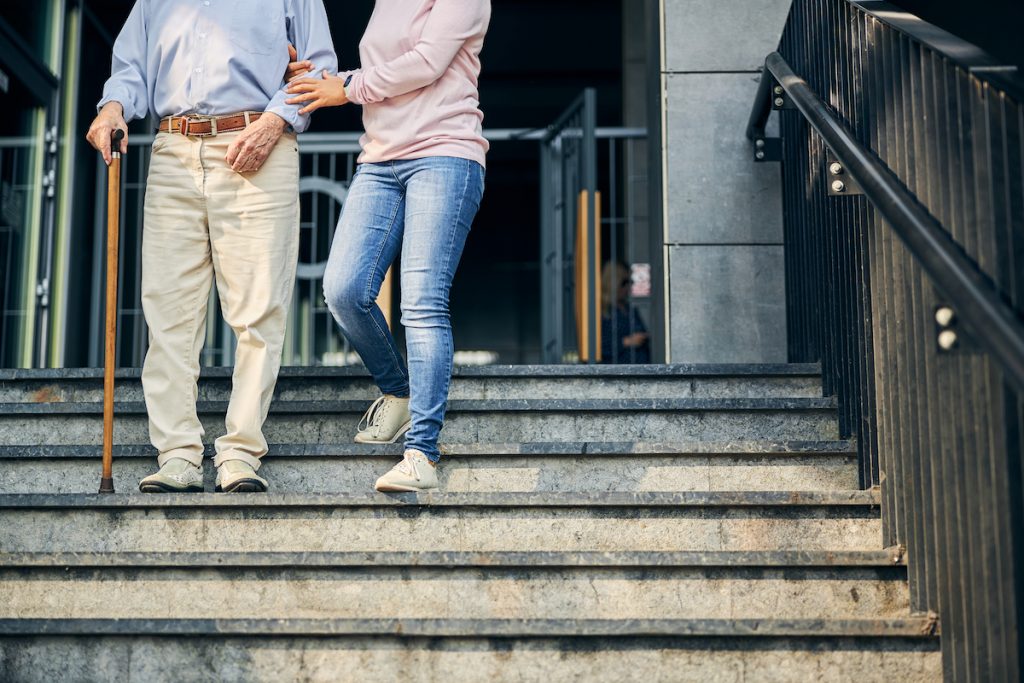 An older man is helped by a friend to walk downstairs after surgery.