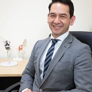 Headshot of Anthony Leong Anthony Leong sitting on desk chair wearing a grey suit