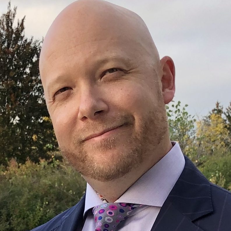 Headshot of Dr. James Howard in a navy blue suit with pink shirt and pink and purple tie